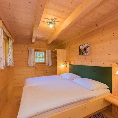Bedroom in the Bed and Breakfast featuring a double bed, wooden walls, exposed ceiling beams, and windows with curtains.