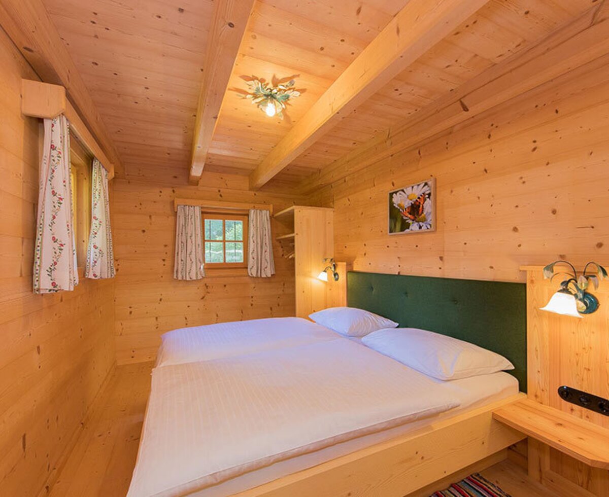 Bedroom in the Bed and Breakfast featuring a double bed, wooden walls, exposed ceiling beams, and windows with curtains.