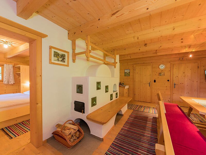 The living area of the Bed and Breakfast features a tiled stove with a bench, a dining area, and access to a bedroom.
