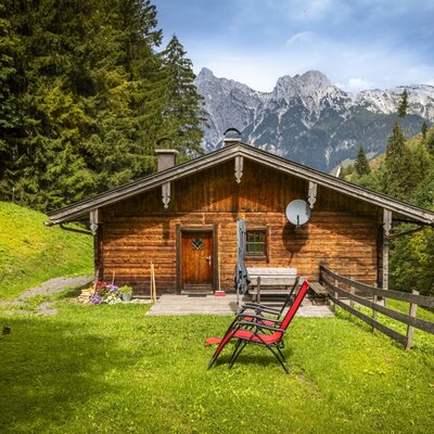The rustic mountain hut  made of warm wood, surrounded by a lush green lawn and impressive mountain peaks.