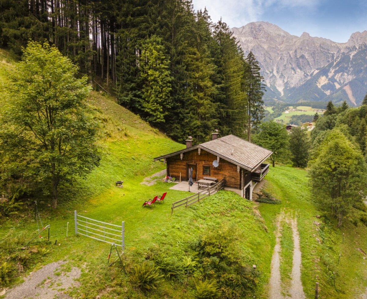 The inviting mountain hut is idyllically nestled on the mountainside, offering expansive views of the surrounding peaks and forests.