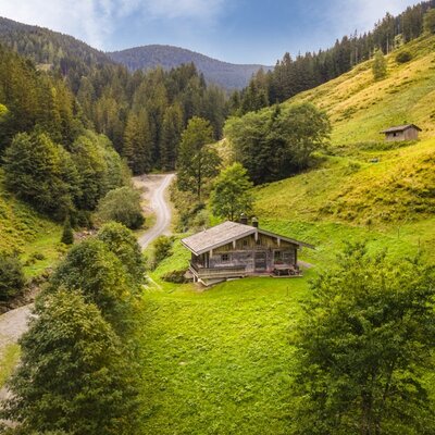 The charming mountain hut  nestled in an idyllic green valley, surrounded by dense forests and rolling mountain slopes.