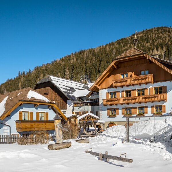 The Farm House buildings and its snow-covered children's play area, set against a winter mountain landscape. The Farm House buildings and its snow-covered children's play area, set against a winter mountain landscape.