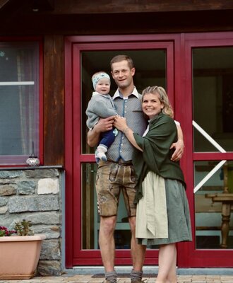 The host family of the Farm House, dressed in traditional attire, stands at the property entrance.