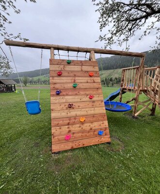 The farmhouse's inviting playground on a green lawn, featuring a climbing wall, swings, and a slide.