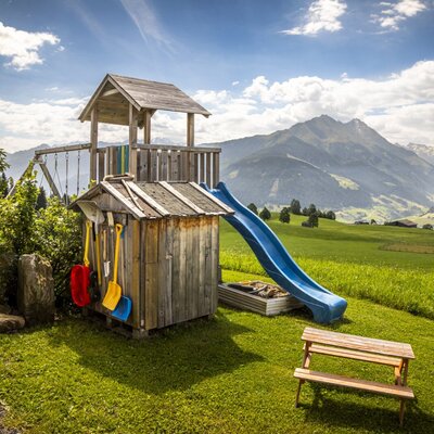 The bed and breakfast's inviting children's playground with a slide and swing set against a picturesque mountain backdrop.
