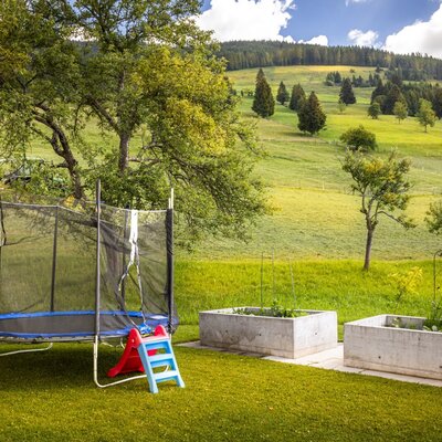 The bed and breakfast's inviting garden featuring a trampoline, raised garden beds, and scenic views of the rolling green hills.