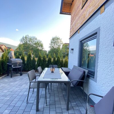 Outdoor paved patio at the farmhouse, featuring a dining table with chairs and a barbecue grill.