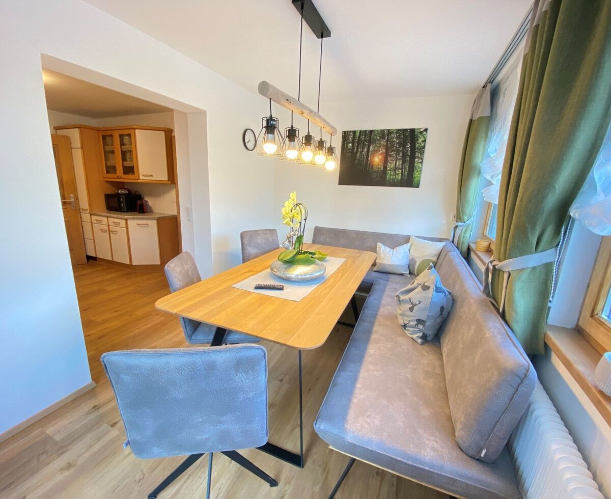 Dining area in the farm house with a wooden table, corner bench seating, additional chairs, and an overhead light fixture, with an adjoining kitchen visible.