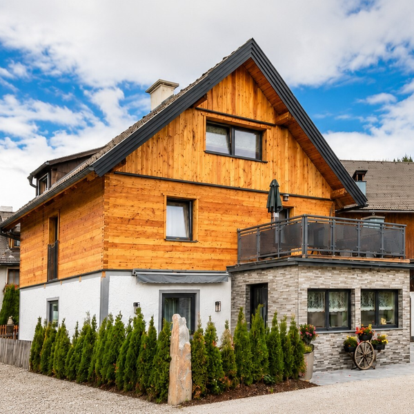 The charming exterior of the farmhouse, featuring a rustic wooden facade, a balcony, and neat green hedges.