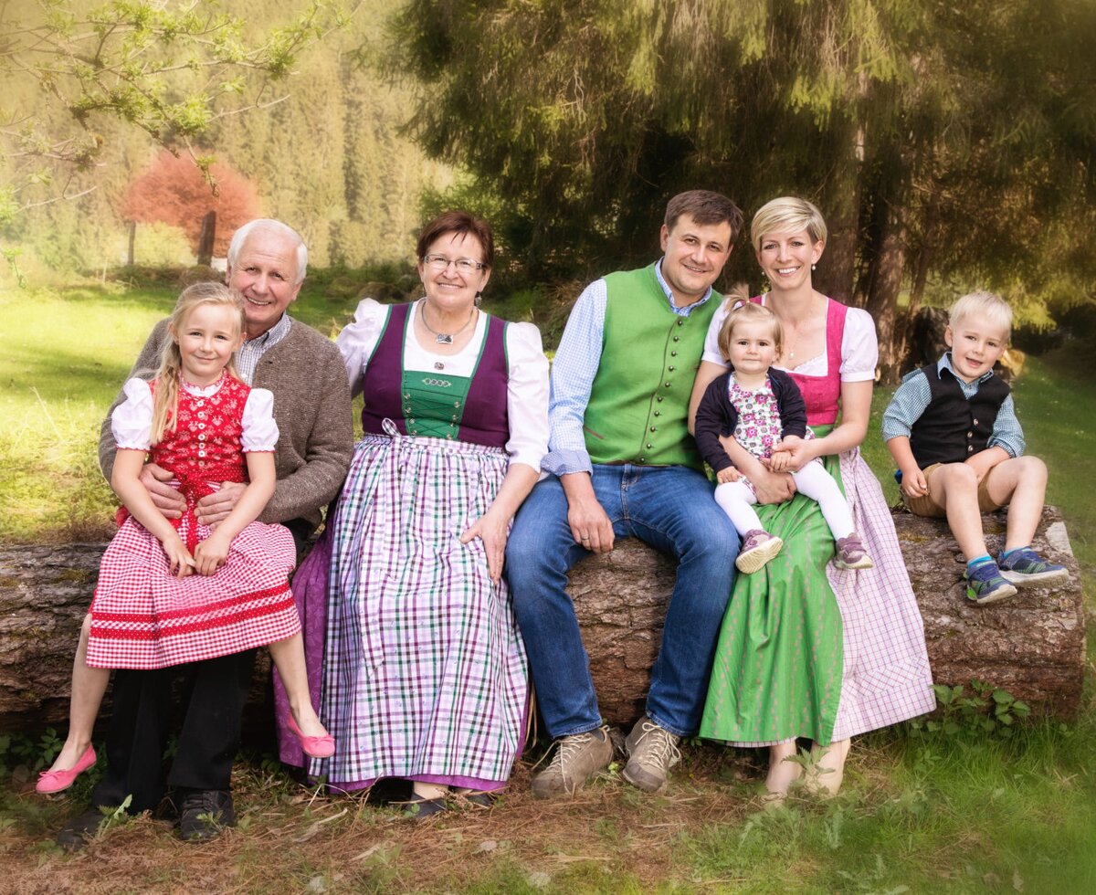 A multi-generational family in traditional clothing sits outdoors at the farmhouse.