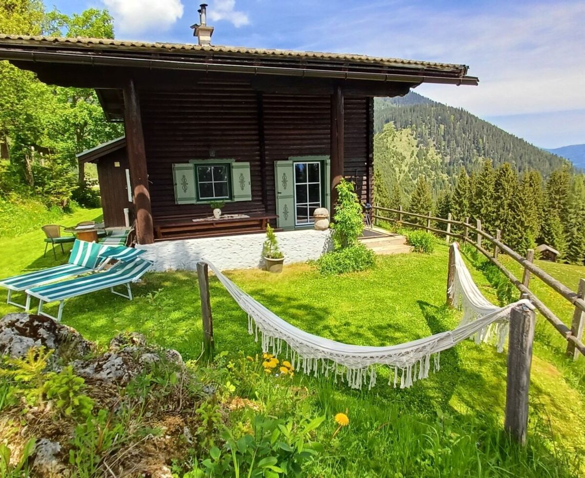 The farmhouse exterior, featuring a terrace with sun loungers and a hammock, overlooks a grassy hillside with mountain and forest views.