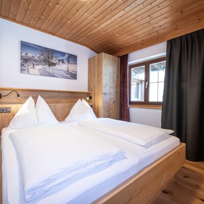 Double bedroom in the apartment featuring a wooden bed with integrated reading lights, a wardrobe, and a window with dark curtains.