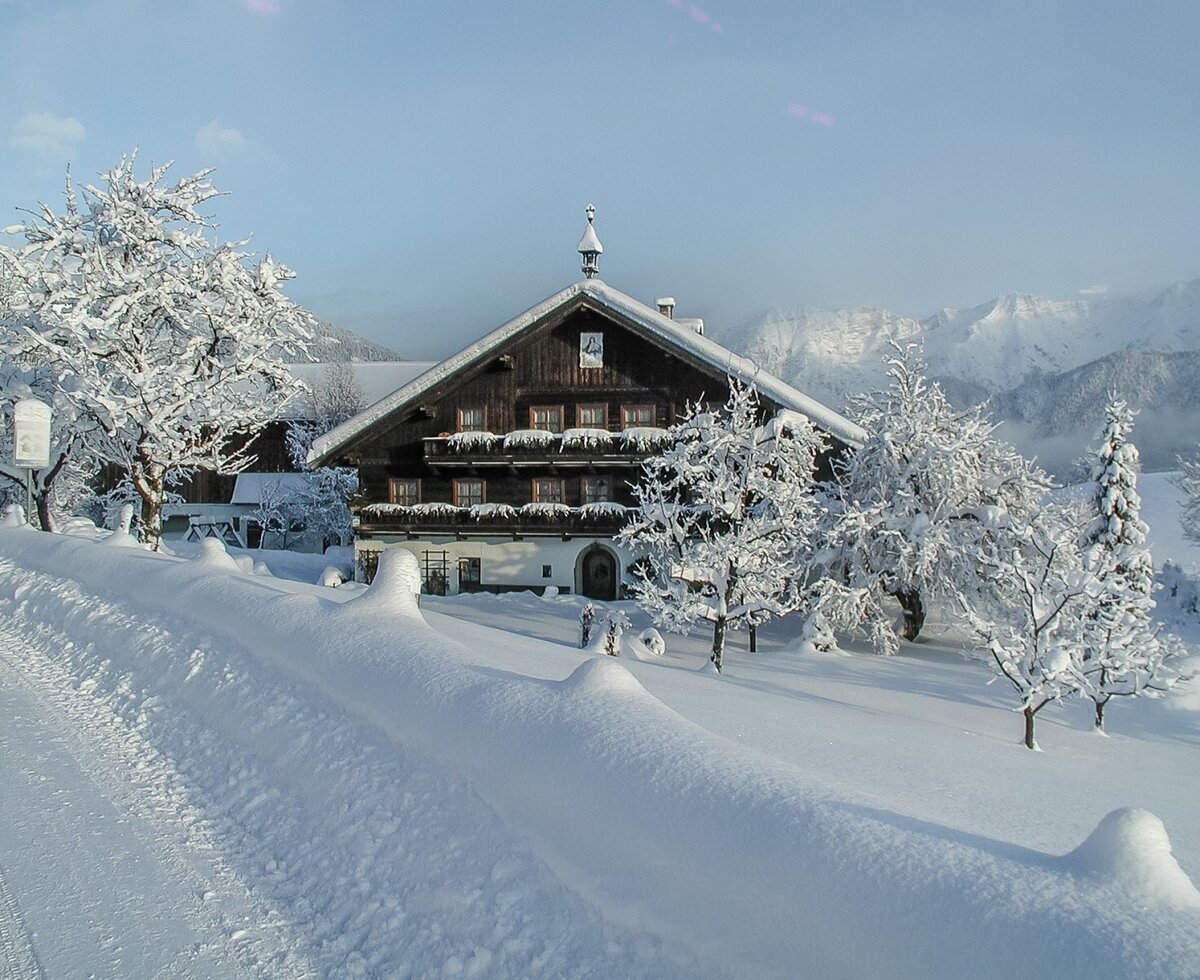 The snow-covered farmhouse in a picturesque winter landscape with views of the surrounding mountains.