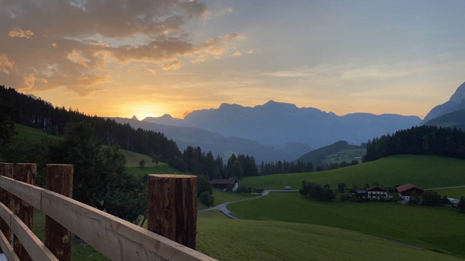 View of the sunset over a mountainous landscape with green fields and houses from the Bed and Breakfast.