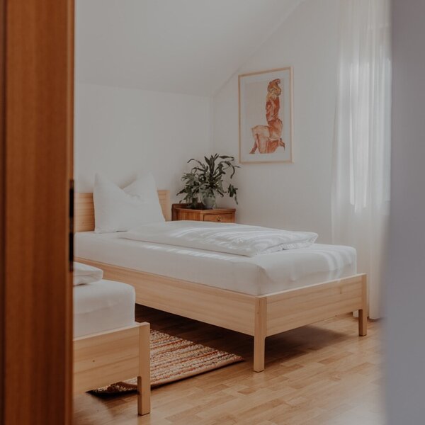 Bedroom in the Farm House with two single wooden-framed beds, white bedding, hardwood floors, a nightstand, and a window with sheer curtains. Bedroom in the Farm House with two single wooden-framed beds, white bedding, hardwood floors, a nightstand, and a window with sheer curtains.