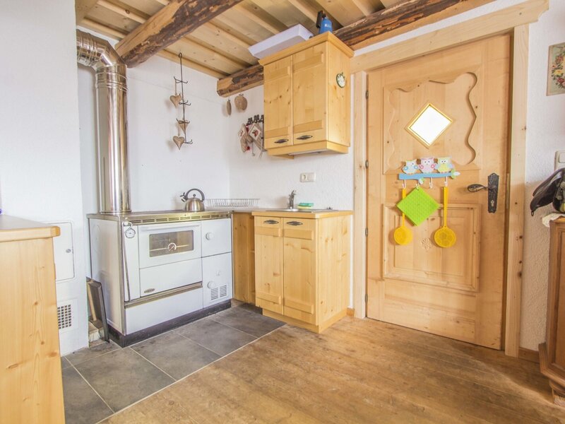 The kitchen area in the farmhouse features a wood-burning stove with an oven, a sink, and wooden cabinetry.