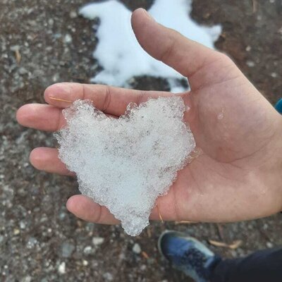 A hand holding snow in the shape of a heart.