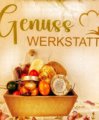 A basket with fresh baked goods, cheese, and eggs, presented under the 'Genuss Werkstatt' sign at the Bed and Breakfast.