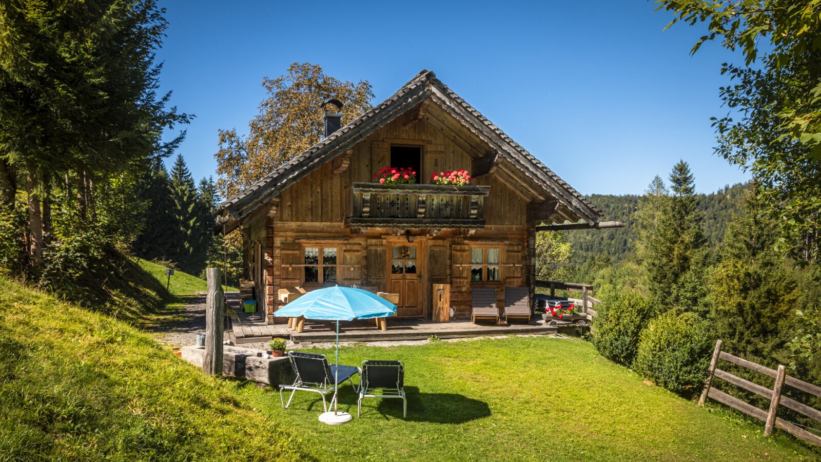 The rustic Almhütte in a secluded location, featuring a sunny garden with loungers and mountain views.