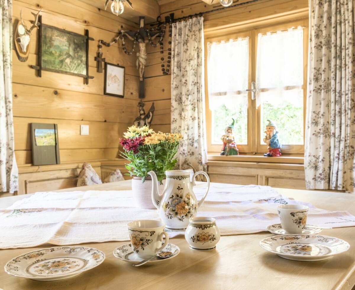 The cozy dining area in the rustic almhut, featuring an invitingly set wooden table with traditional floral tableware.
