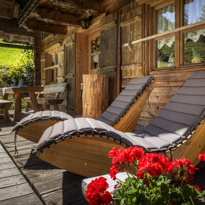 The alm's inviting wooden terrace, featuring comfortable sun loungers and colorful geraniums.