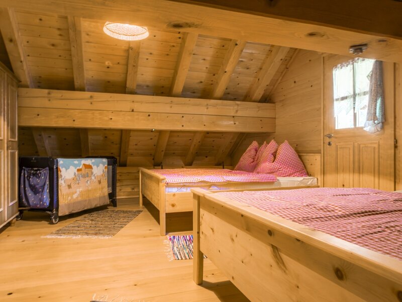 A cozy bedroom in the almhut featuring traditional wooden furniture, checkered bedding, and a convenient baby cot.