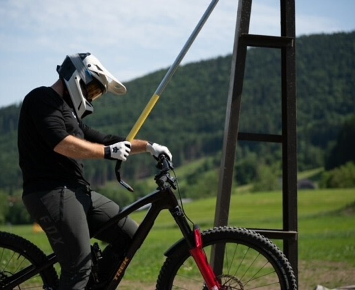 A mountain biker with protective gear uses a T-bar lift to ascend the mountains.