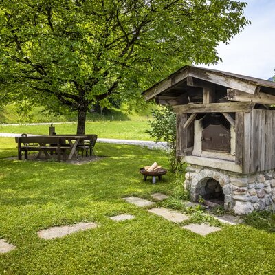 The Farm House garden features an outdoor oven, a fire pit, and a picnic area under a large tree.