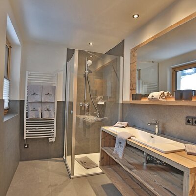 Farm House bathroom featuring a walk-in shower, a wooden vanity with a sink, a large mirror, a hairdryer, and a heated towel rail.