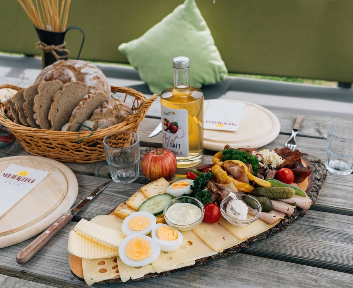 A hearty snack platter at the farmhouse featuring fresh bread, cheese, cold cuts, and apple juice on a rustic wooden table.