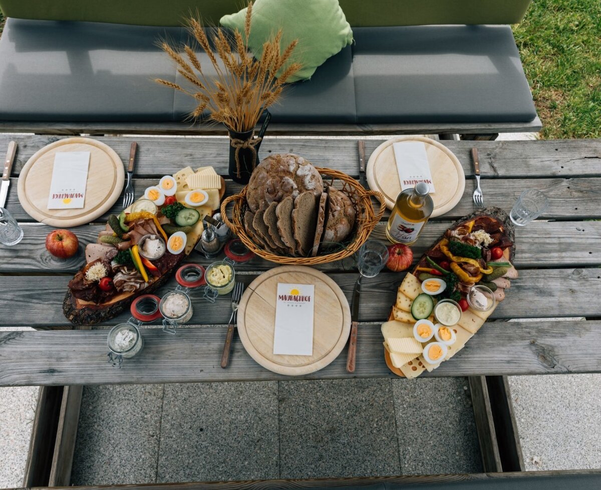 A hearty, traditional snack board with fresh bread, cheese, and cold cuts served on a rustic wooden outdoor table at the farmhouse.
