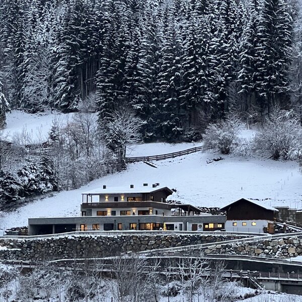 The Farm House exterior in winter, surrounded by snow-covered pine forests and mountains.