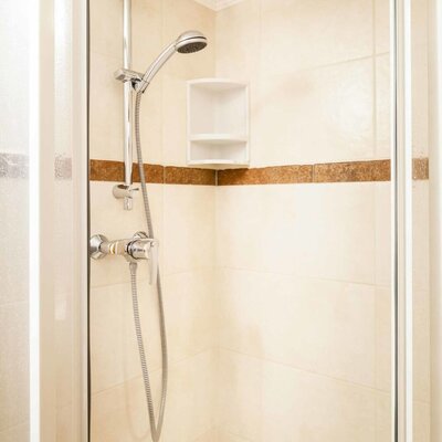Tiled shower cabin in the farmhouse bathroom equipped with an adjustable shower head and a corner shelf.