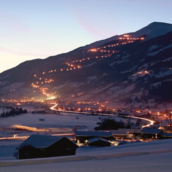 View from the farm house showing the illuminated mountain valley and village, with light trails on the slopes and a winding road. View from the farm house showing the illuminated mountain valley and village, with light trails on the slopes and a winding road.