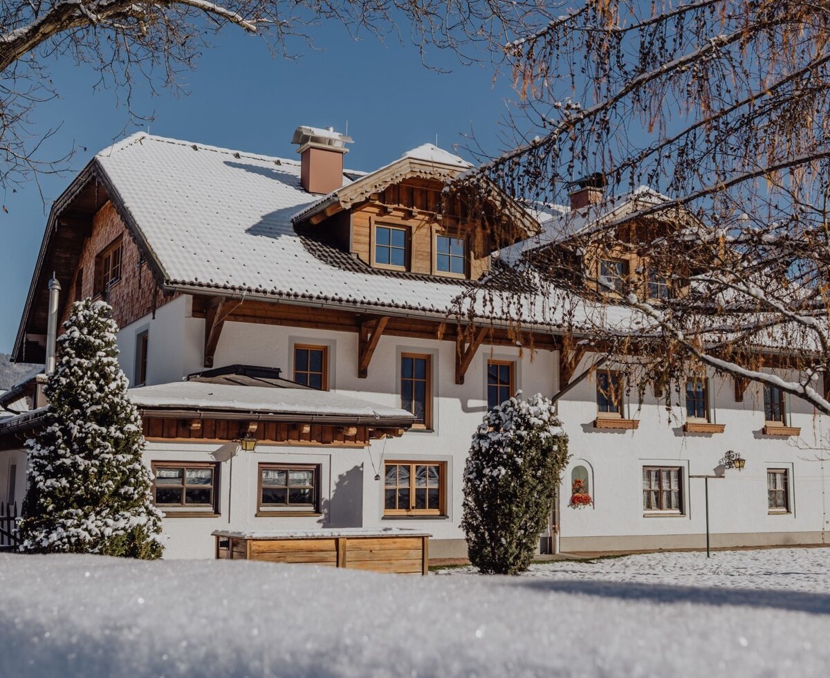 The farmhouse in winter with a snow-covered roof and snowy surroundings.