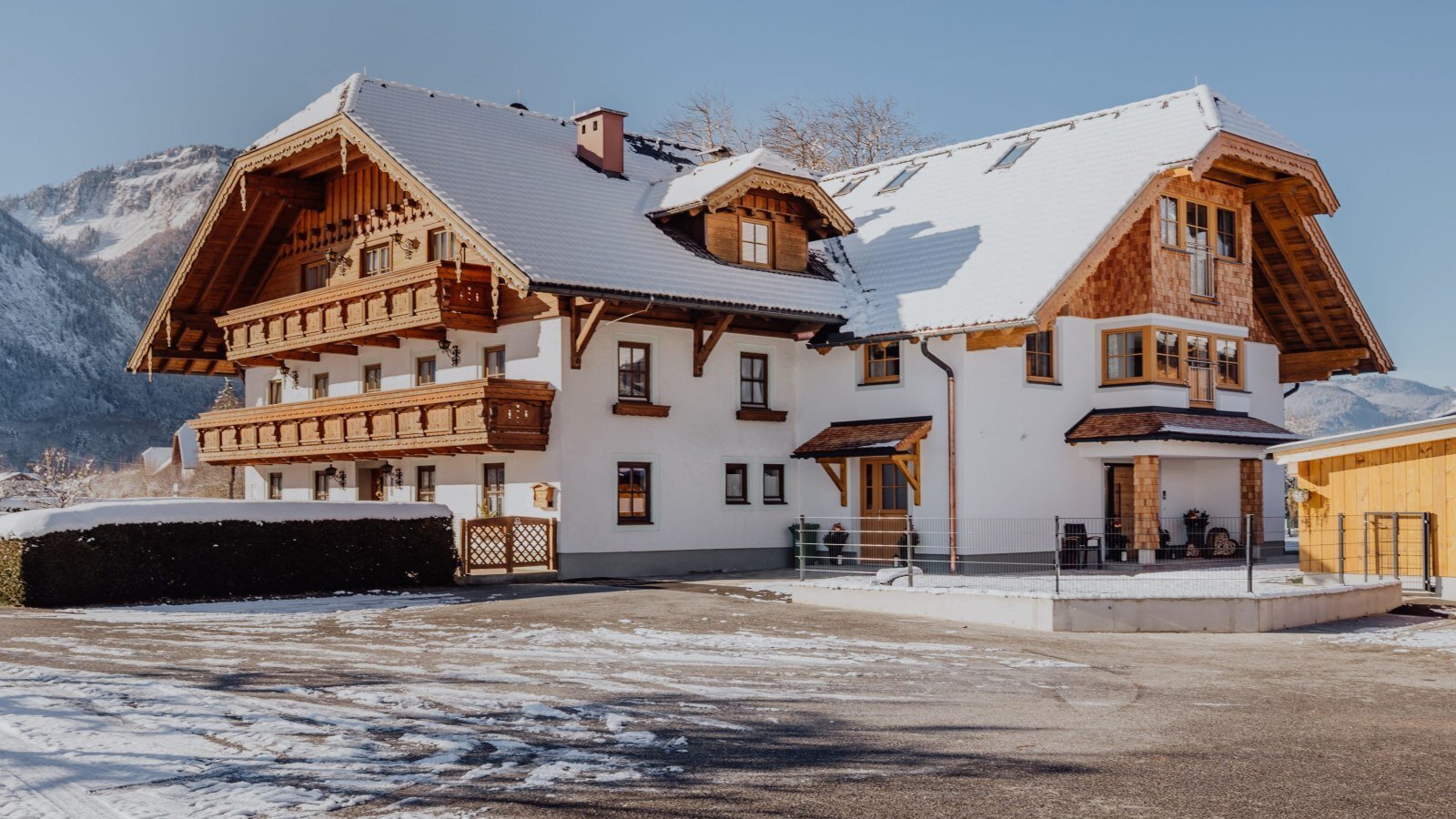 The farmhouse in winter, featuring a snowy roof and wooden balconies against a mountain backdrop.