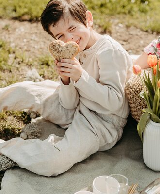 A child holding a heart-shaped food item on a picnic blanket, indicating family-friendly outdoor activities at the farm house.