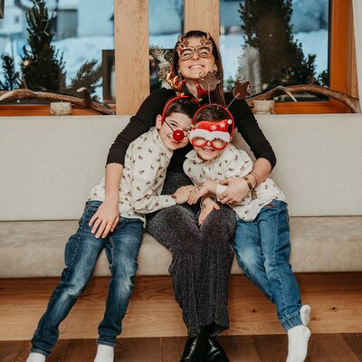 A family with a mother and two children sitting on a bench in the farmhouse, all wearing festive accessories.