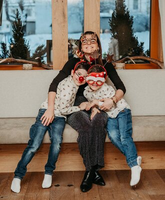 A family with a mother and two children sitting on a bench in the farmhouse, all wearing festive accessories.