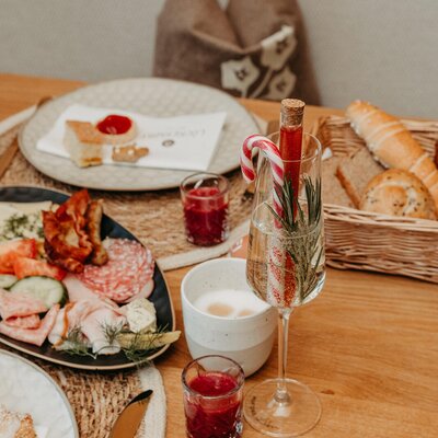 A set breakfast table at the farmhouse featuring cold cuts, pastries, cake, and a champagne glass with rosemary and a candy cane.