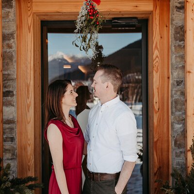 The entrance to the farmhouse, adorned with mistletoe and fir greenery, with a couple in front and a view of the snow-covered mountains.