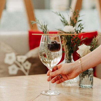 A guest holding a cocktail glass garnished with rosemary and a small bottle in the Bauernhof's lounge area.