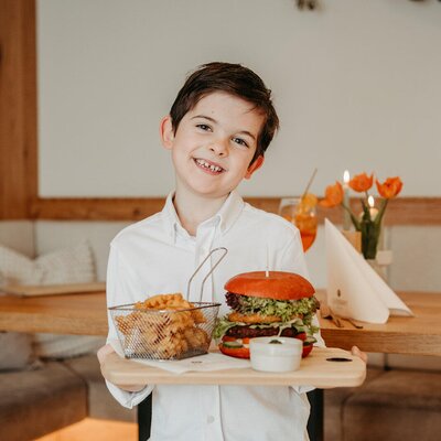 A child presents a burger with french fries in a dining area of the farmhouse.