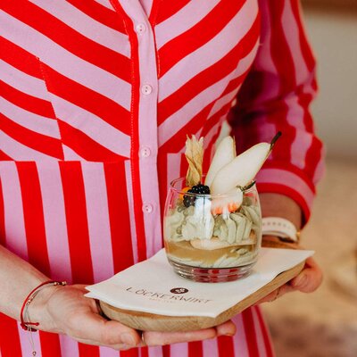 A layered dessert with fruit and cream in a glass, served on a branded tray from the farmhouse.