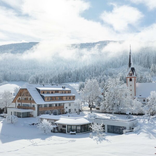 The exterior of the Farm House, Löckerwirt, within a snow-covered village, featuring a prominent church and winter forest scenery. The exterior of the Farm House, Löckerwirt, within a snow-covered village, featuring a prominent church and winter forest scenery.