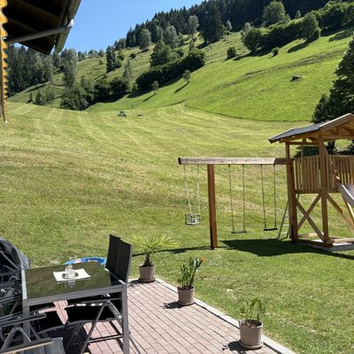 The inviting terrace with a shaded seating area, a children's playground, and views of the mountain slopes.