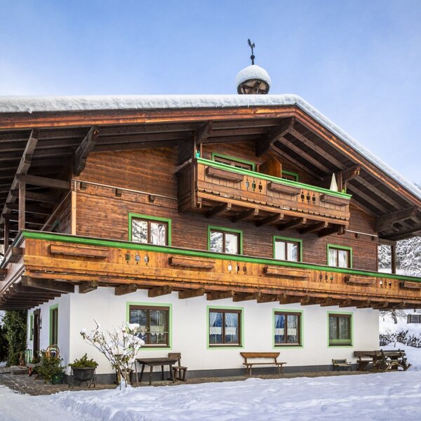 The exterior of the Farm House, featuring wooden upper floors, white lower walls, and balconies, surrounded by snow.