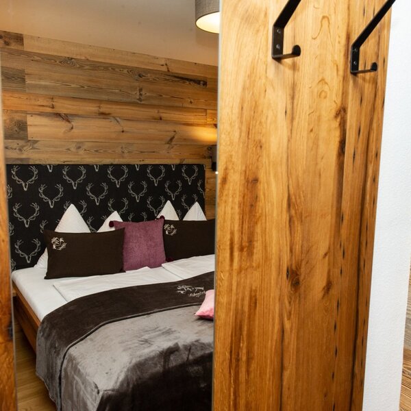 Double bedroom in the Farm House featuring a bed with a patterned headboard, wooden wall paneling, and a sliding wooden door with coat hooks.