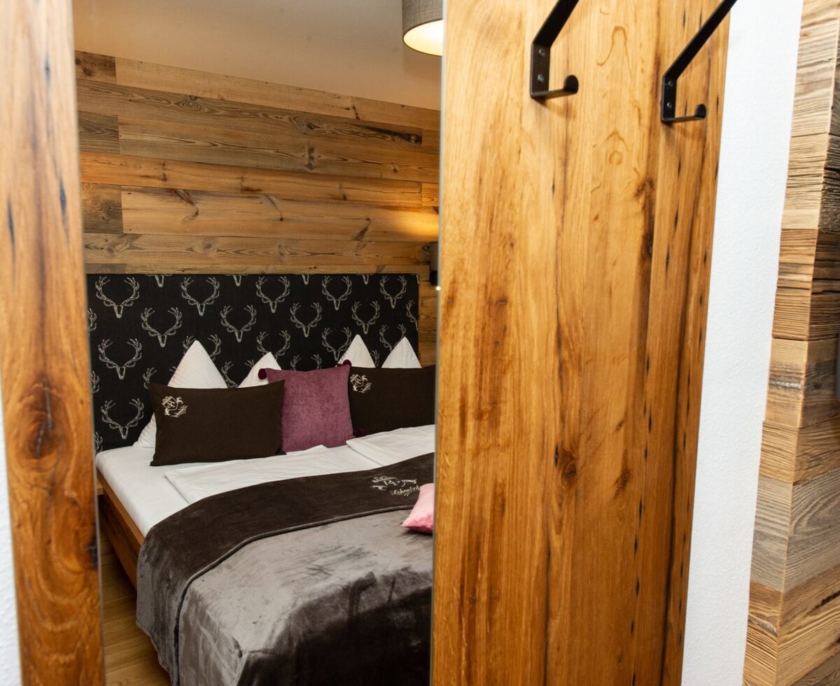 Double bedroom in the Farm House featuring a bed with a patterned headboard, wooden wall paneling, and a sliding wooden door with coat hooks.